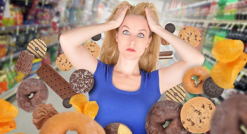 A woman has sweet food snacks around her on in a grocery store. She has fear and there are donuts and cookies. Use it for a health or diet concept.